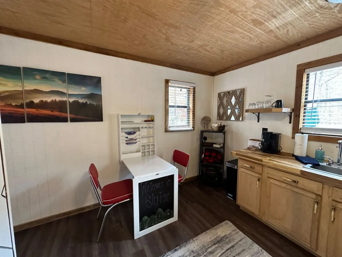 A cozy dining area adjacent to the kitchenette, furnished with vibrant red chairs and a small dining table. Wall art and compact kitchen appliances are visible, reinforcing the space's functionality for both meal preparation and casual dining.