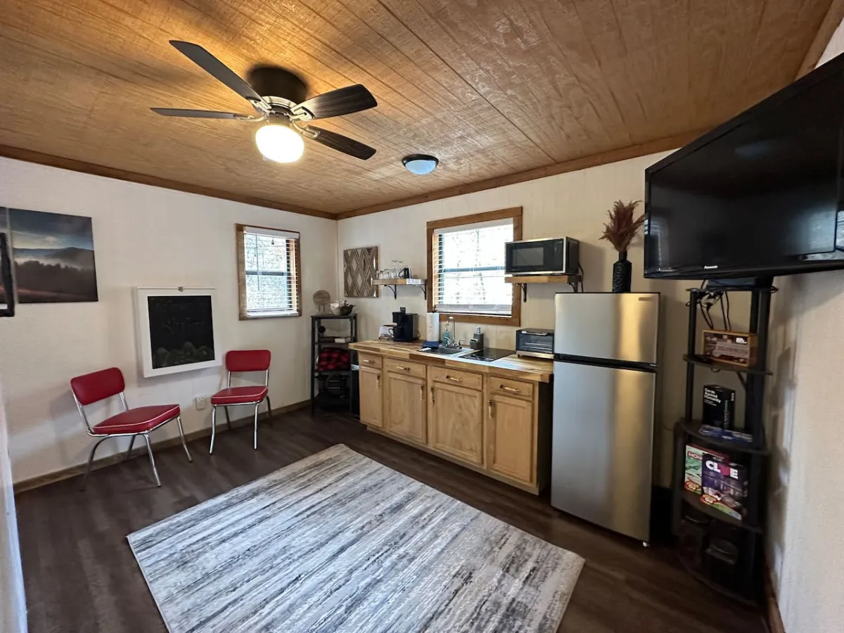 A bright kitchenette featuring a prominent retro red fridge/freezer, compact stove, microwave, and coffeemaker. The area also includes red chairs and wall artwork, creating a lively yet welcoming atmosphere. Plenty of natural light filters in, enhancing the inviting feel of the space.