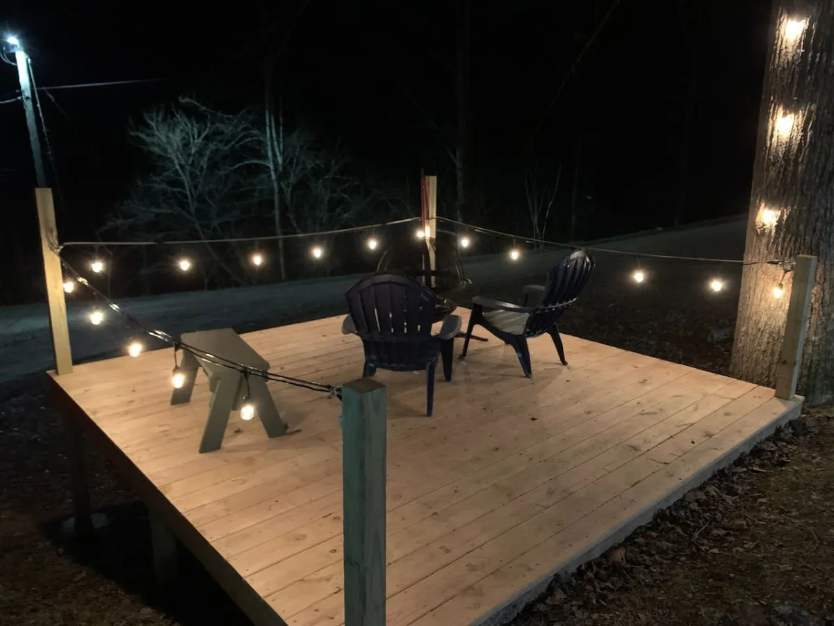 The hero image showcases the exterior of the 'Sly Fox' luxury tiny cabin, warmly lit by string lights with inviting Adirondack chairs placed on a wooden deck. This cozy setting sits against a backdrop of peaceful Smoky Mountain nature, evoking a sense of tranquility and intimate relaxation ideal for couples or solo travelers.