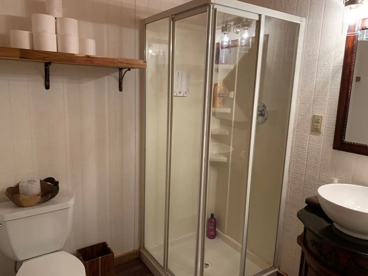 A modern bathroom featuring a glass shower enclosure, a sleek vanity with a bowl sink, and practical shelving with towels and toiletries. The space feels fresh and functional.